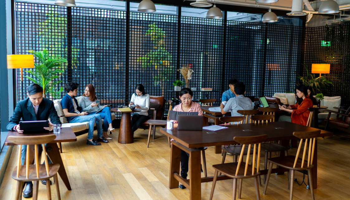 Un espace de bureau convivial avec plusieurs personnes assises soit à des tables avec leur PC portable ou dans des sofas.